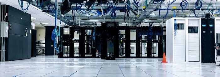 Data center room with rows of racks, raised floor and overhead cabling