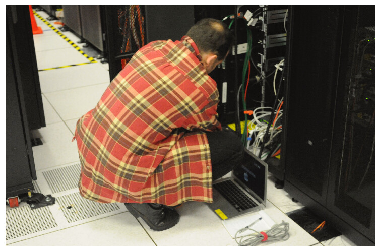 Technician performing maintenance on a server rack in a data center, with a laptop connected for diagnostics