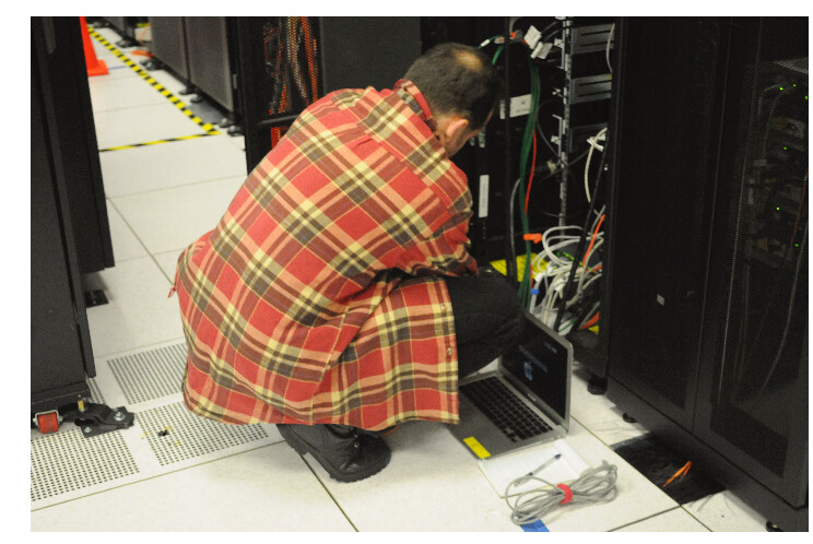 Técnico realizando mantenimiento en un rack de servidores en un data center, con laptop conectado para diagnóstico